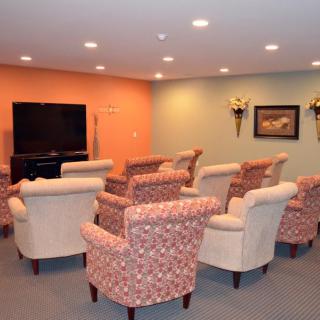 A cozy seating area with multiple chairs facing a television, accented by an orange wall and decorative elements.