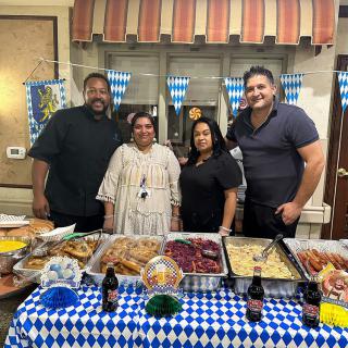 A group of four people posing in front of a buffet table with various dishes indoors.