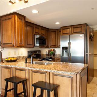 A modern kitchen with wooden cabinets, a granite countertop island, and stainless steel appliances.