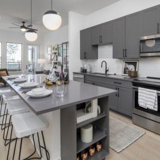 A modern kitchen with gray cabinets and an island counter equipped with bar stools and pendant lighting.