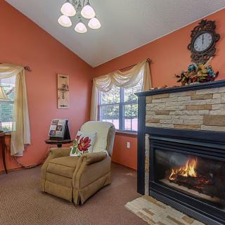 A cozy living room with an armchair by the fireplace, featuring orange walls and a large window.