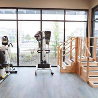 A rehabilitation center with various exercise equipment and a wooden staircase for physical therapy exercises.