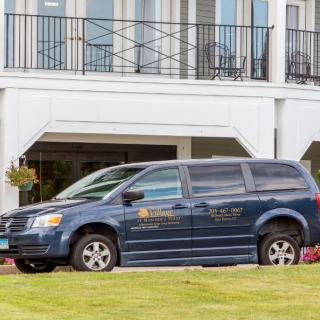 A blue van parked in front of a white building.
