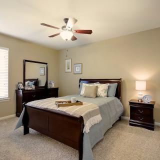 A cozy bedroom with a well-made bed, nightstand, and mirror in a warmly lit interior.