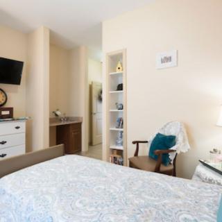 A cozy and well-decorated bedroom featuring a bed with patterned bedding, a wall-mounted TV, a bookshelf, and a comfortable chair.