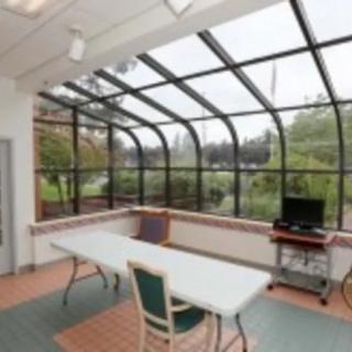 A bright and airy sunroom with a glass roof, featuring a table and chairs, overlooking a garden.