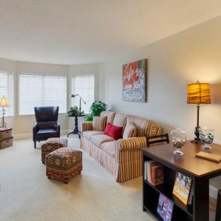 A cozy living room with a sofa, armchair, and a desk, warmly lit by lamps.