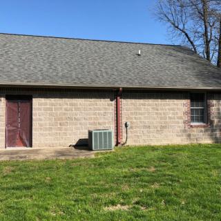 A brick residential building with a sloped roof and a grassy yard.