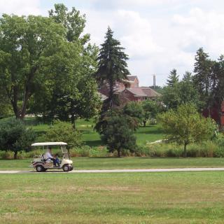 A golf cart drives down a path surrounded by trees and grass in a park-like setting.
