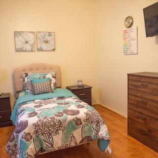 A cozy bedroom with a single bed featuring colorful bedding, a wall-mounted TV, and stylish decor.