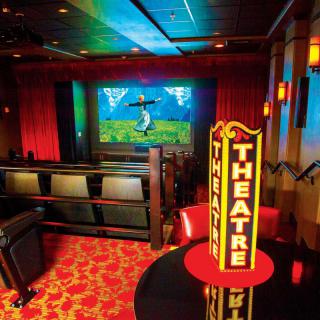 A colorful theater interior with seating and a stage adorned with bright lighting and a prominent 'Theatre' sign.