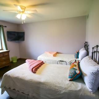 A bright bedroom with two twin beds, a ceiling fan, and a wall-mounted television.