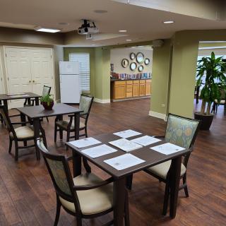 A cozy dining area with neatly arranged tables and chairs, featuring modern decor and a refrigerator in the background.