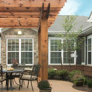 A cozy patio with a wooden pergola, featuring outdoor furniture and potted plants.