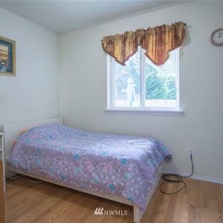 A small bedroom with a single bed, window with curtains, and hardwood flooring.