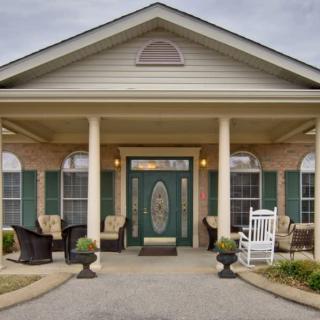 A charming front porch with columns, rocking chair, and potted plants leading to a residential entrance.