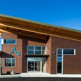 A modern building with a sloped roof and wood exterior, featuring large windows and a main entrance.