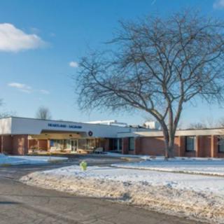 A school building with a snowy landscape and leafless tree in the foreground.