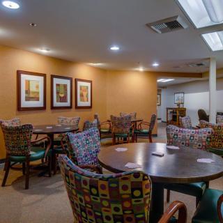 A cozy dining area with multiple tables and colorful chairs, decorated with framed artwork on the walls.