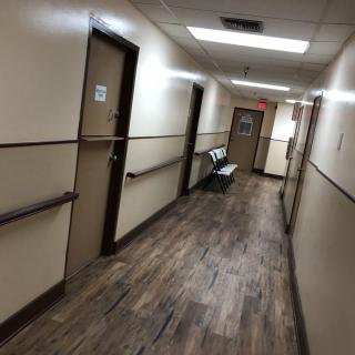 A dimly lit hospital hallway with doors on either side and seating at the end.