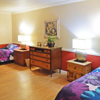 A cozy bedroom featuring twin beds with floral bedding, illuminated by table lamps on wooden nightstands against a warm-toned wall.