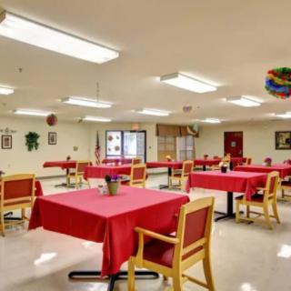 A community dining room with tables covered in red tablecloths and decorated walls.