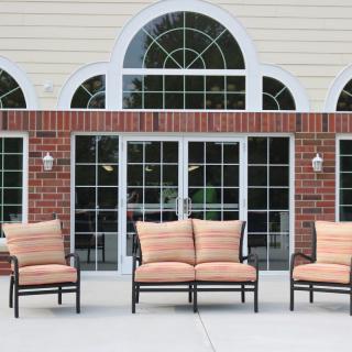 Outdoor patio area with cushioned furniture in front of large windows and a brick wall.