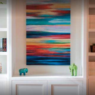 Colorful abstract painting displayed on a shelf with decorative figurines.