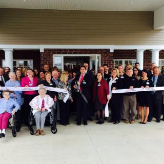 A group of people participating in a ribbon-cutting ceremony outdoors.