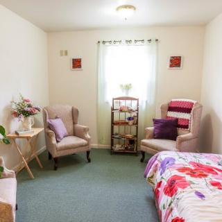 A cozy bedroom with two armchairs, a bed with floral bedding, and bright natural light.