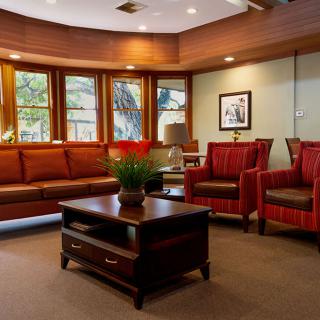 A cozy living room with comfortable seating, a central coffee table, and natural light streaming through large windows.
