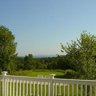 A scenic view of a lush green landscape with trees and a white fence under a clear blue sky.