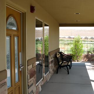 A sunny porch with a bench, door, and windows overlooking a fenced area.