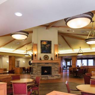 A cozy dining area with a central fireplace, wooden ceiling beams, and soft lighting.