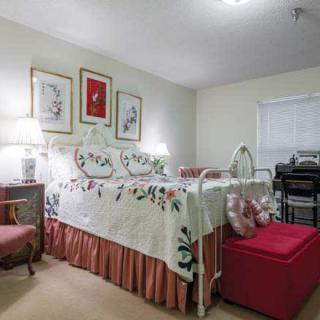 A cozy bedroom featuring a decorative quilt-covered bed, warm lighting from lamps, and artwork on the walls.