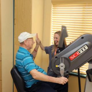 A therapist high-fives a patient during a rehabilitation session using exercise equipment.