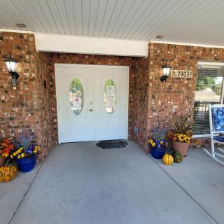 A welcoming front porch with double doors, brick walls, and decorative potted plants.