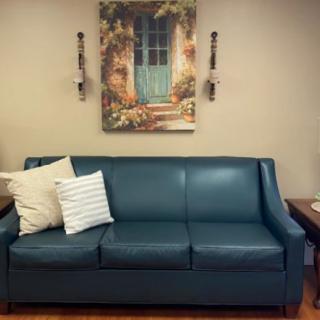 A cozy living room setup featuring a teal sofa with decorative pillows and a scenic painting above.