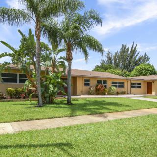A suburban house with a well-manicured lawn and palm trees on a sunny day.