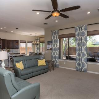 A spacious living room with modern decor, featuring a ceiling fan, sofas, and an open view to the kitchen.