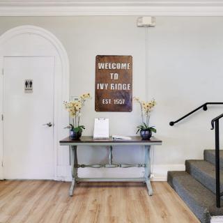 A welcoming interior with a sign, decorative plants, and a table near the stairs.