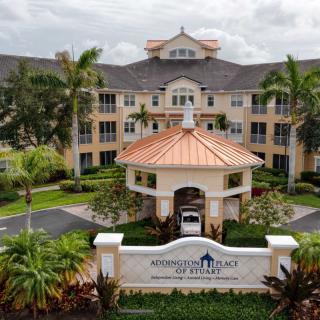 A scenic view of an elegant building surrounded by lush landscaping and palm trees, featuring a prominent entrance and sign.
