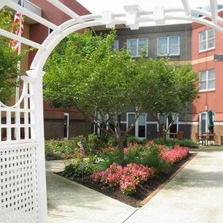 A beautiful courtyard garden with flowers and an archway in front of a brick building.