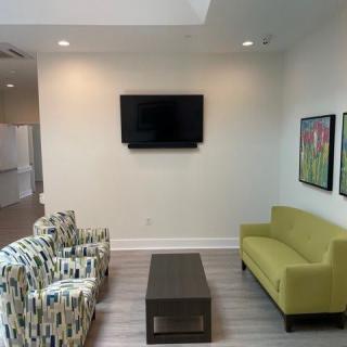 A modern living room with a green sofa, patterned armchairs, and a wall-mounted television.