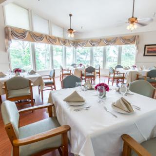 A beautifully arranged dining room with tables set for a meal, featuring large windows that allow natural light to brighten the space.