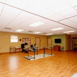 A spacious rehabilitation room with exercise equipment and parallel bars on a wooden floor.
