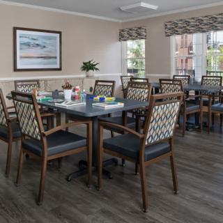 A well-lit dining room with neatly arranged tables and chairs, featuring large windows and tasteful decor.