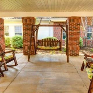 A cozy porch area featuring a wooden swing and rocking chairs, framed by brick pillars.