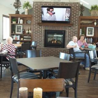 A cozy lounge area with people sitting around tables, a brick fireplace, and a television mounted above.