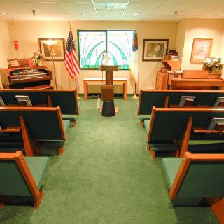Interior view of a small chapel with rows of seating, podium, and flags.